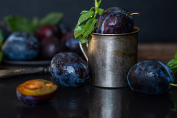 Plums with leaves on a black stone plate. Rustic food background. Fresh organic fruits. Healthy food. Toned image. Free space for your text.