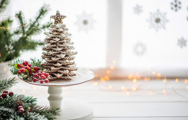 The handmade eatable gingerbread and New Year Tree with decoration. Gingerbread over defocused magic light winter window. Wonderful holiday mood. Copy space for your text.