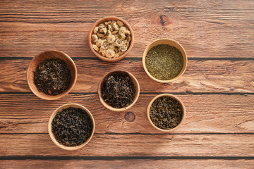 assortment of dry tea in white bowls on wooden surface