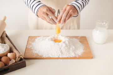 Egg poured into flour during the baking process, man's hands