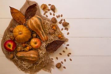 Autumn background with yellow, green, brown leaves, red apples and pumpkins. Vegetables harvest on rustic wooden table with copy space. Mockup for seasonal offers and holiday postcard, top view.