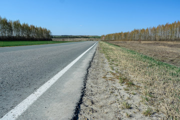 A winding highway stretching into the distance against the backdrop of a beautiful spring landscape, fields, meadows, forests and hills. Road stripes on asphalt.