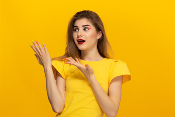Close-up portrait of a beautiful young girl pointing with a finger at the copyspace for product advertisement isolated over yellow background.