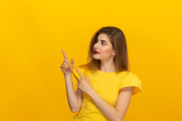 Close-up portrait of a beautiful young girl pointing with a finger at the copyspace for product advertisement isolated over yellow background.