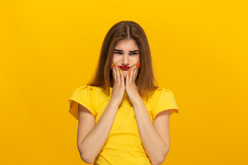 Beautiful young woman with long hair stands upset isolated over yellow background.