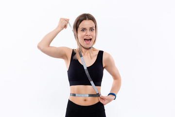 Fototapeta na wymiar Young blond woman in a black sportswear with smart watches is happy checking waist after workout with the tape measure standing over white background.