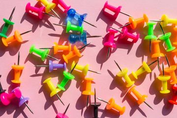 Creative school flat lay top view.Set of push pins of different colors on a pink background with shadows and hard light, school art background