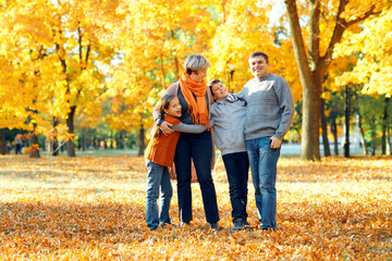 Happy family posing, playing and having fun in autumn city park. Children and parents together having a nice day. Bright sunlight and yellow leaves on trees, fall season.