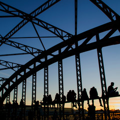 Munich / Germany - February 16 2019: Silhouettes of people sitting on the railing of a railway bridge at sunset