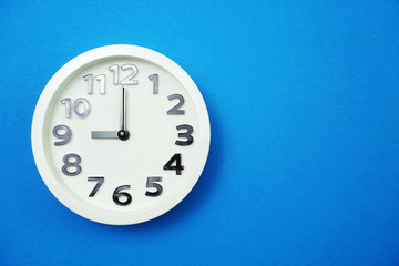 Fototapeta na wymiar White round clock showing Nine o'clock on blue background