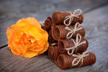Handmade apple pastille rolled and tied with linen thread on a wooden background with an orange rose