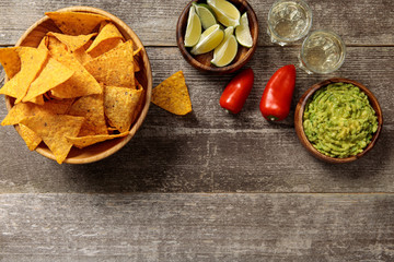 top view of nachos served with guacamole, peppers, limes and Tequila on weathered wooden table