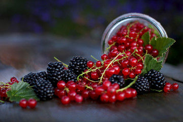  Ripe blackberry and red currant in a glass jar on a wooden background