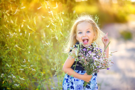 playful cute little girl playing outdoors at sunset, holding a bouquet of wildflowers and having fun, happy childhood