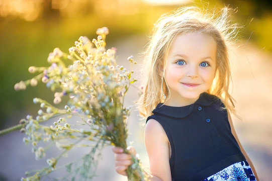 playful cute little girl playing outdoors at sunset, holding a bouquet of wildflowers and smiling, happy childhood