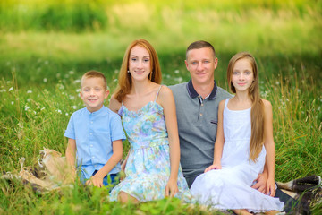 Fototapeta premium portrait of a happy family outdoors, sitting together on the grass hugging and smiling, family spends time together