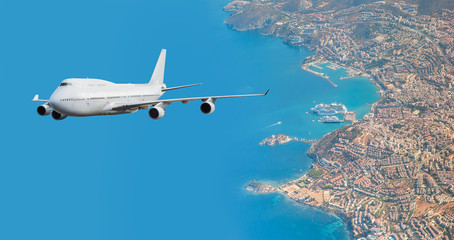 Fototapeta na wymiar Commercial white Airplane Flying Over City and Blue sea