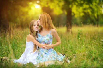 Fototapeta na wymiar portrait of a happy mother with her daughter, sitting in the park on the grass, hugging and smiling, mother gently kisses her daughter, happy motherhood