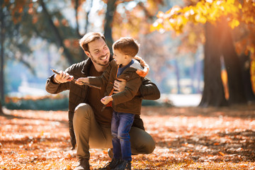 Happy father and little son playing and having fun outdoors over autumn park background