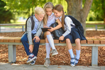 school friends, schoolchildren sitting on a bench in the park use a tablet, social media communication