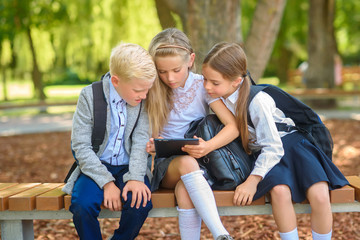 school friends, schoolchildren sitting on a bench in the park use a tablet, social media communication