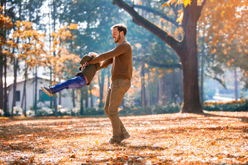 Happy father and little son playing and having fun outdoors over autumn park background