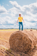 Naklejka na ściany i meble British red-haired cheerful boy stands on a haystack in the field and inspects his farm holdings
