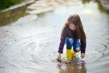 cute little girl in yellow boots plays in a puddle with a wooden boat, childhood, autumn concept
