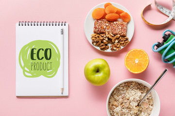 top view of fresh diet food, measuring tape, skipping rope and notebook with eco product lettering on pink background