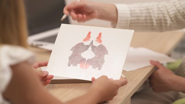Close-up of a psychologist showing Rorschach inkblot image to her teenage patient and writing down the results. Selective focus shot