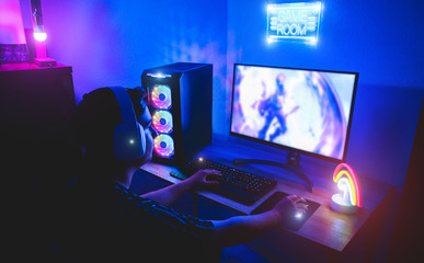 Young gamer playing online platform with neon lights in background - Male guy having fun gaming and streaming in internet with pc - Technology game trends, entertainment concept - Focus on right hand