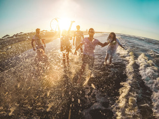 Happy friends having fun on the beach at sunset - Young people playing inside sea water outdoor in...