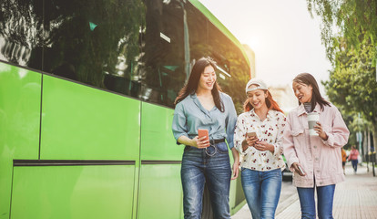 Happy asian friends using smartphones at bus station - Young students people having fun with technology trends after school outdoor - Friendship, university and trasports app concept - Focus on faces © DisobeyArt