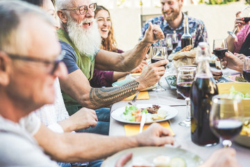 Happy family eating and drinking wine at barbecue dinner on patio outdoor - Mature and young people having fun at bbq sunday meal - Food and summer lifestyle concept - Focus on hipster man arm hand