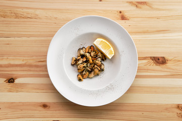 Plate with marinated mussels and slice of lemon on wooden table