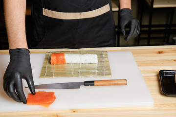 Male hand put salmon while preparing rolls