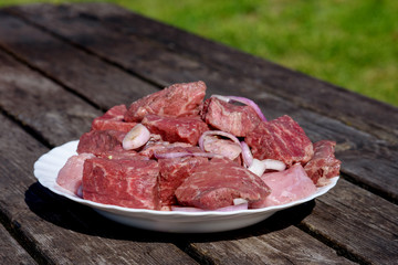 Cooking on fresh air. The plates with fresh meat is standing on the wooden table in the countryside getting ready for preparing.