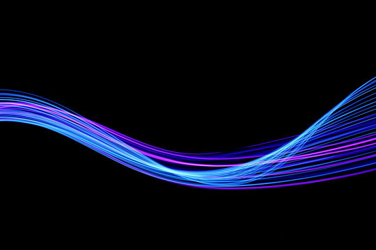 Long exposure, light painting photography.  Vibrant streaks of neon blue and pink color against a black background.