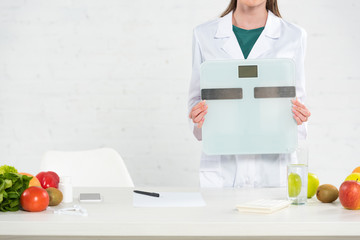 cropped view of dietitian in white coat holding digital scales