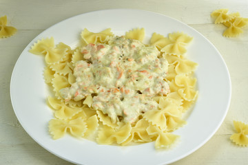 Farfalle pasts with salmon and cheese sauce on a white plate. Wooden background. Top view.