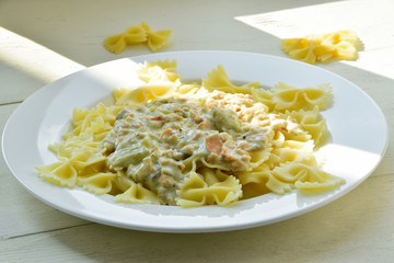Farfalle pasts with salmon and cheese sauce on a white plate. Wooden background.