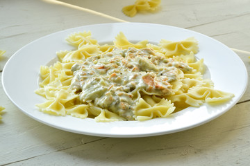 Farfalle pasts with salmon and cheese sauce on a white plate. Wooden background.