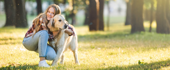 panoramic shot of beautiful young girl in casual clothes hugging golden retriever while sitting on...