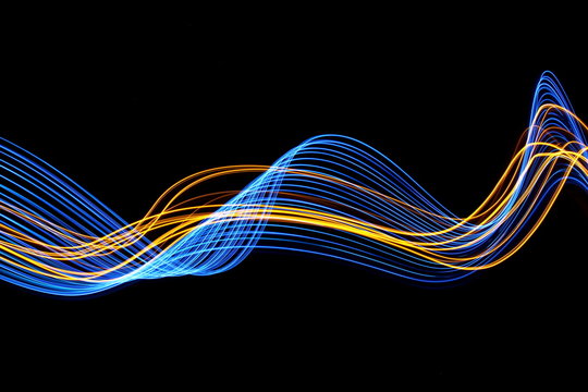 Long exposure, light painting photography.  Vibrant streaks of neon blue and gold color against a black background.
