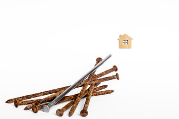 A shiny metal nail lies on a pile of old rusty nails and is aimed at the house symbol on a white background.