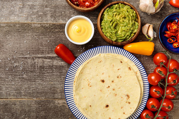 top view of Mexican tortilla with guacamole, cheese sauce and salsa on weathered wooden table with copy space