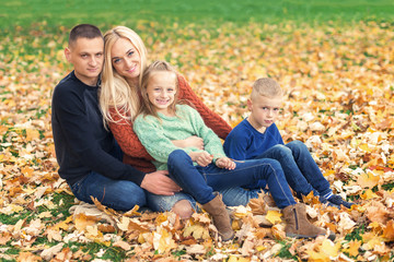 Fototapeta premium Happy family resting in beautiful autumn park. Parents with two children in autumn leaf.