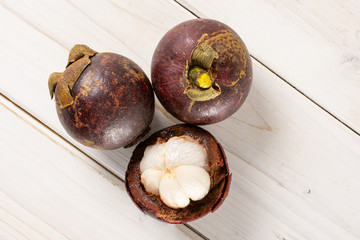 Group of two whole one half of deep purple mangosteen flatlay on white wood