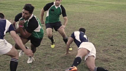 Men playing a game of rugby on a sports field, blocking and falling to have possession of ball. Rugby players in action on pitch during the match