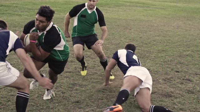 Men playing a game of rugby on a sports field, blocking and falling to have possession of ball. Rugby players in action on pitch during the match